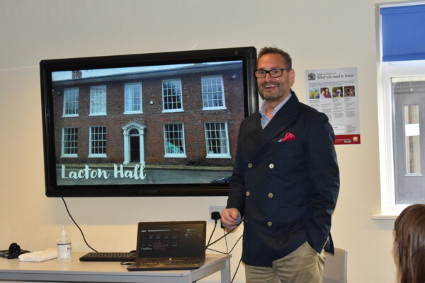 man stood in front of screen picture of lacton hall